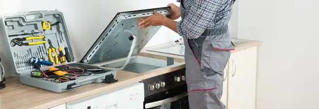 Cooktop repair technician lifting a built-in stovetop for service in Fort Collins, CO