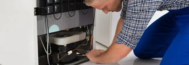 Refrigerator repair technician servicing the compressor and condenser area in Fort Collins, CO