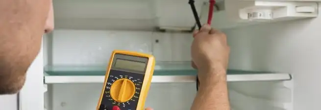 Refrigerator repair technician testing electrical components with a multimeter in Fort Collins, CO