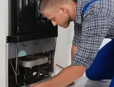 Refrigerator repair technician servicing the compressor and condenser area in Fort Collins, CO